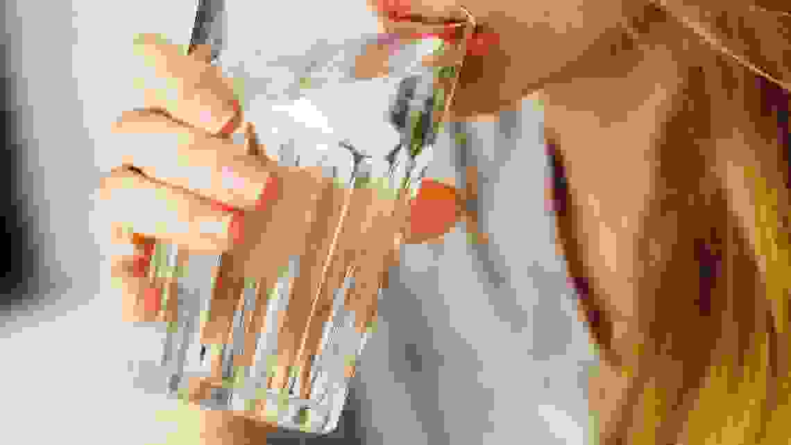 En kvinna med blont hår och grå t-shirt dricker ur ett glas med vatten. Man ser bara halva hennes ansikte.