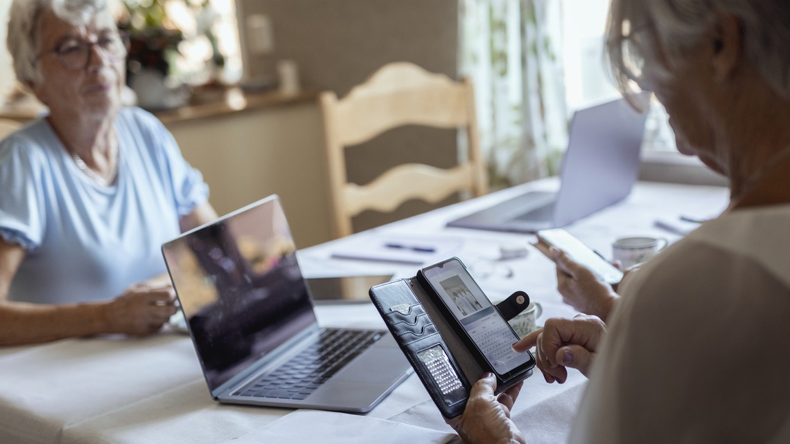 Äldre kvinnor sitter vid dator och mobiltelefon