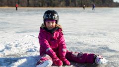 Flicka med hjälm och skridskor sitter på isen