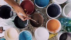 Färgburkar i olika färger och en hand som håller i en pensel. 