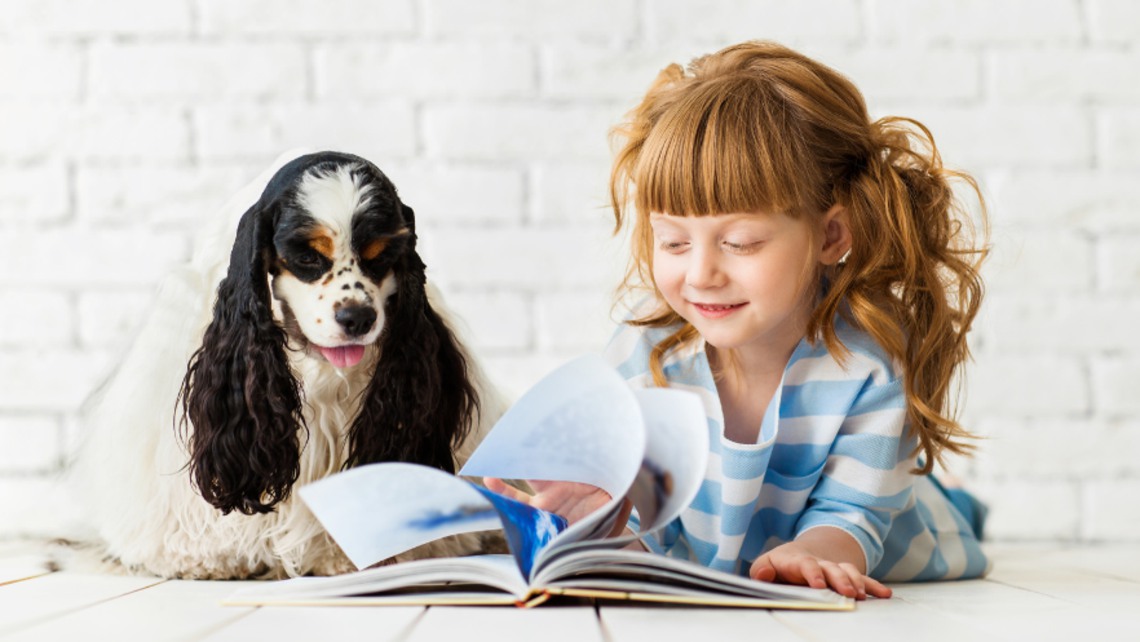 En flicka och en hund tittar i en bok tillsammans.